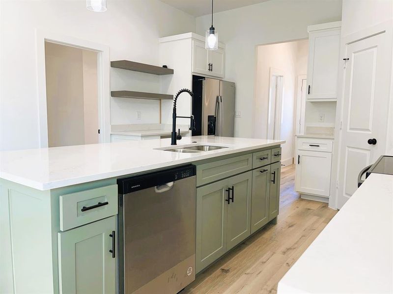 Kitchen featuring appliances with stainless steel finishes, light wood-type flooring, green cabinets, pendant lighting, and white cabinets