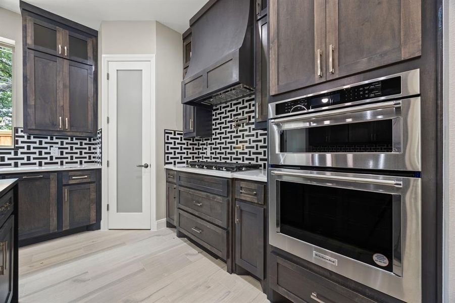 Kitchen featuring dark brown cabinets, stainless steel appliances, custom range hood, and tasteful backsplash