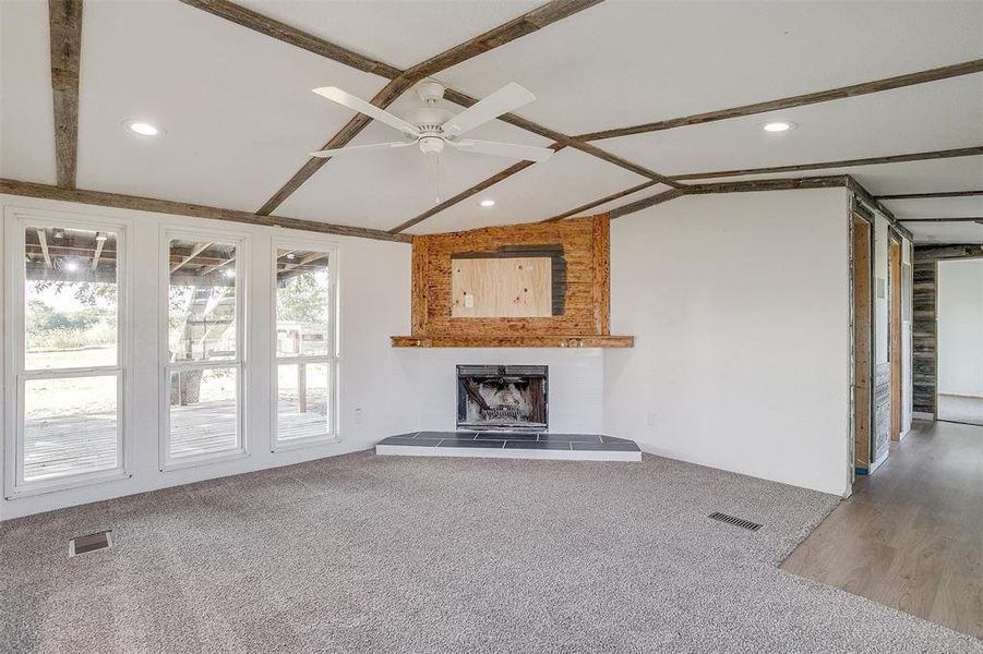 Unfurnished living room featuring ceiling fan, lofted ceiling with beams, wood-type flooring, and a fireplace