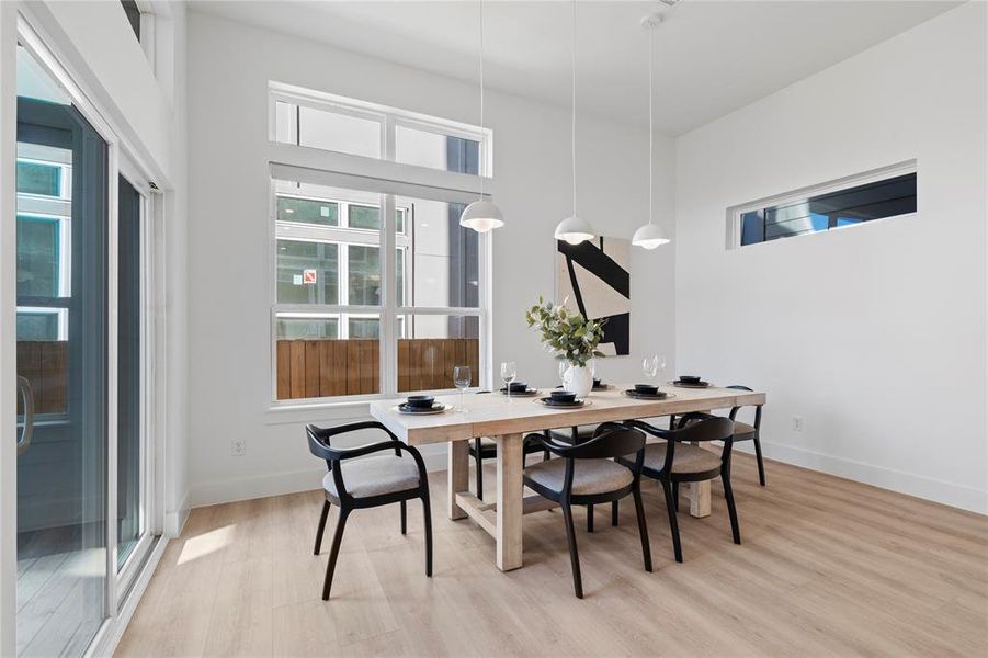 This inviting dining space is bathed in natural light, thanks to the expansive windows and sliding glass doors that open to the outdoors. The sleek, modern pendant lights above the table add an elegant touch, making this the perfect setting for casual meals or formal gatherings, with easy access to outdoor entertaining.