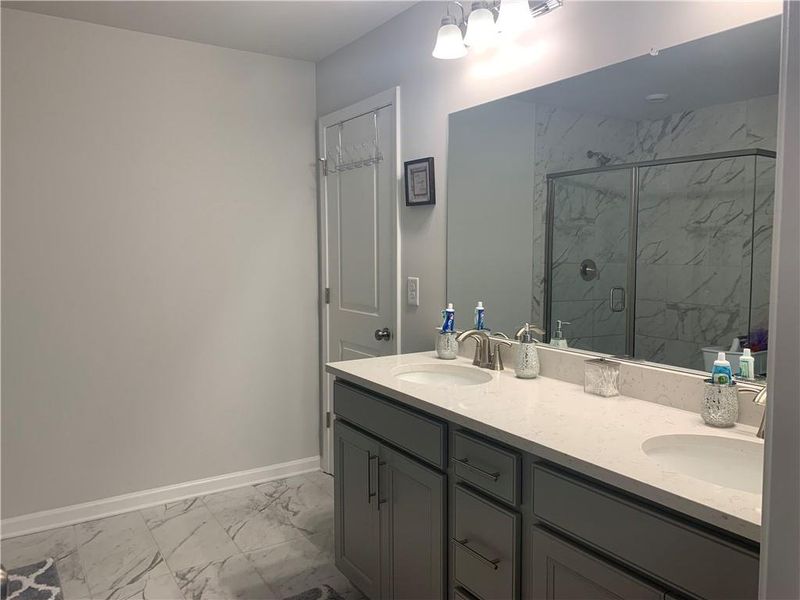 Bathroom with tile flooring, double sink vanity, and a shower with door