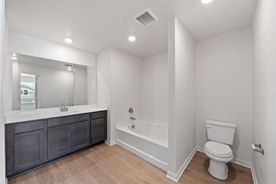 Bathroom with wood-style floors, a bath, toilet, and vanity