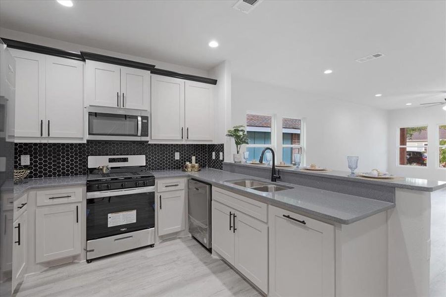 Kitchen with appliances with stainless steel finishes, sink, light wood-type flooring, and kitchen peninsula