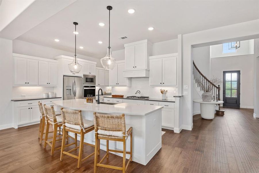 Kitchen with backsplash, dark hardwood / wood-style flooring, appliances with stainless steel finishes, and a center island with sink