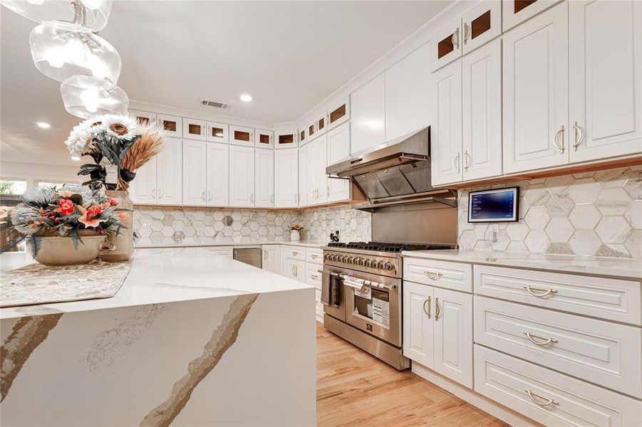 Kitchen with white cabinets, backsplash, light stone countertops, light wood-type flooring, and double oven range