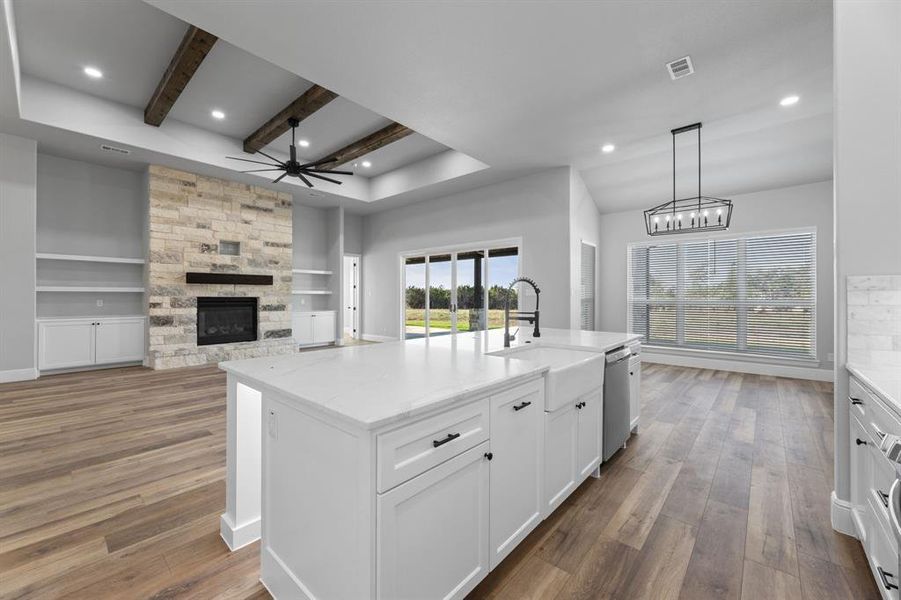 Kitchen with view of kitchen island with sink, pendant lighting, white cabinetry, and a fireplace