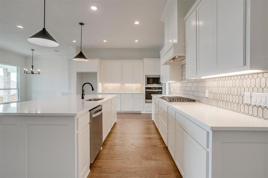 Kitchen featuring a large island with sink, sink, ornamental molding, white cabinets, and appliances with stainless steel finishes