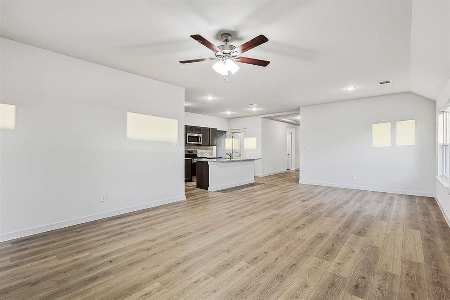 Unfurnished living room with lofted ceiling, sink, ceiling fan, and light hardwood / wood-style flooring