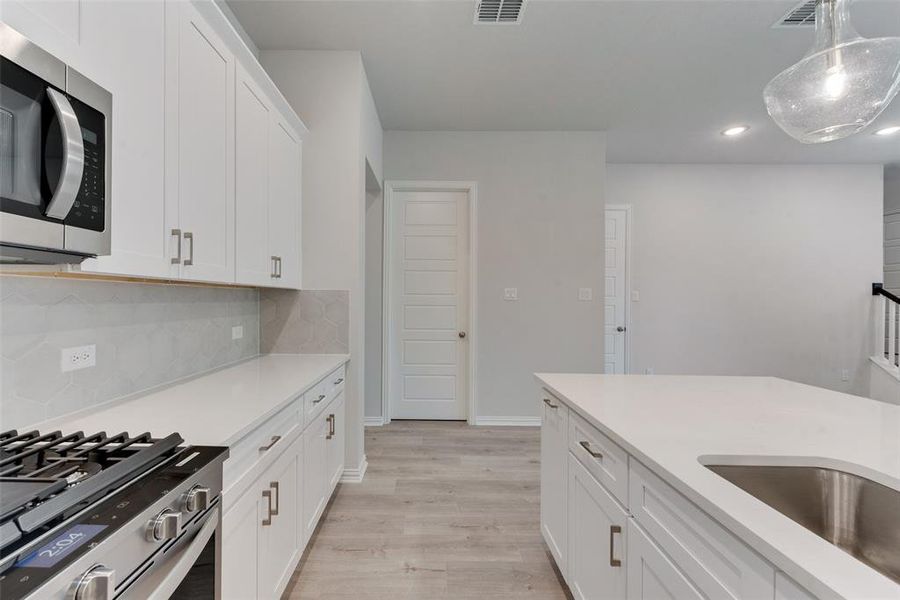 Kitchen with appliances with stainless steel finishes, backsplash, decorative light fixtures, light wood-type flooring, and white cabinetry