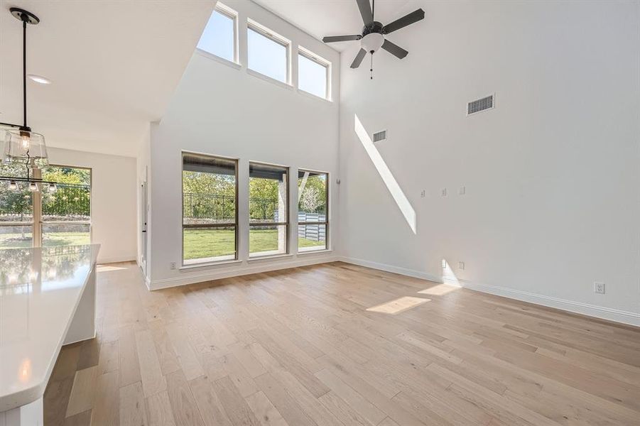 Unfurnished living room with ceiling fan with notable chandelier, a towering ceiling, and light hardwood / wood-style floors