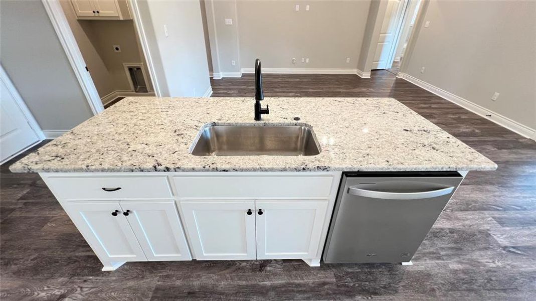 Kitchen featuring light stone counters, sink, a center island with sink, white cabinetry, and dishwasher