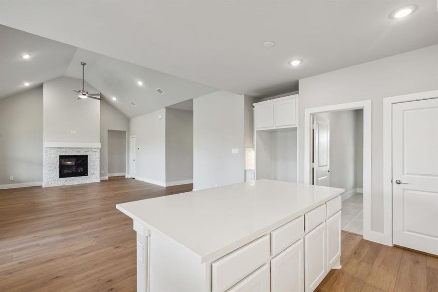 Kitchen featuring white cabinets, light hardwood / wood-style flooring, a center island, a fireplace, and vaulted ceiling