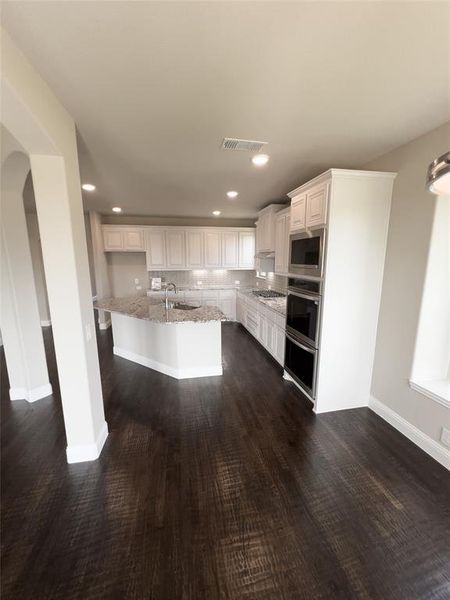 Kitchen featuring dark hardwood / wood-style flooring, appliances with stainless steel finishes, an island with sink, white cabinetry, and sink