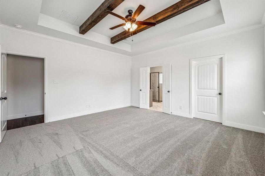 Carpeted empty room with crown molding, ceiling fan, a raised ceiling, and beam ceiling
