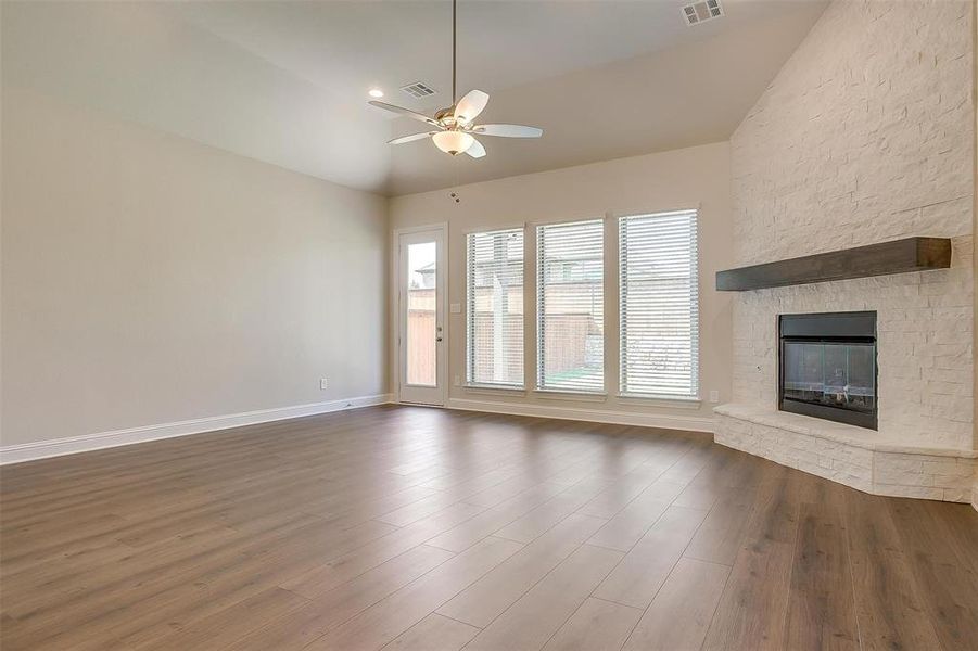 Unfurnished living room featuring hardwood / wood-style floors, high vaulted ceiling, a stone fireplace, and ceiling fan