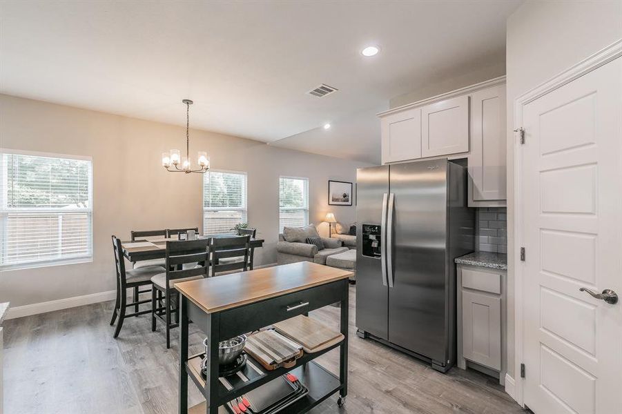 Kitchen with light wood-type flooring, an inviting chandelier, decorative light fixtures, stainless steel refrigerator with ice dispenser, and tasteful backsplash