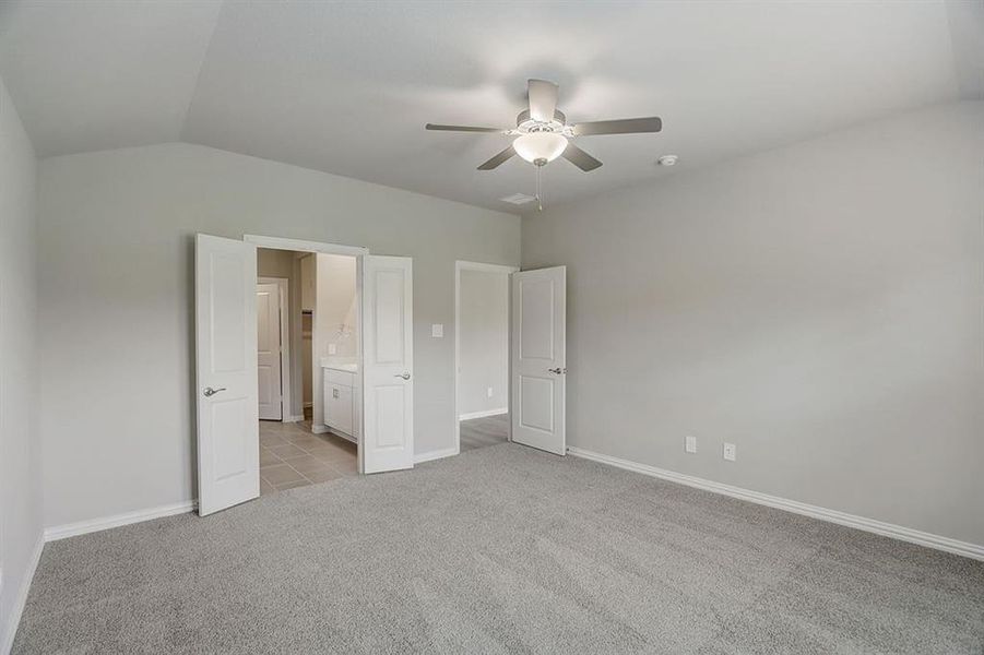 Unfurnished bedroom with vaulted ceiling, ceiling fan, light carpet, and ensuite bathroom