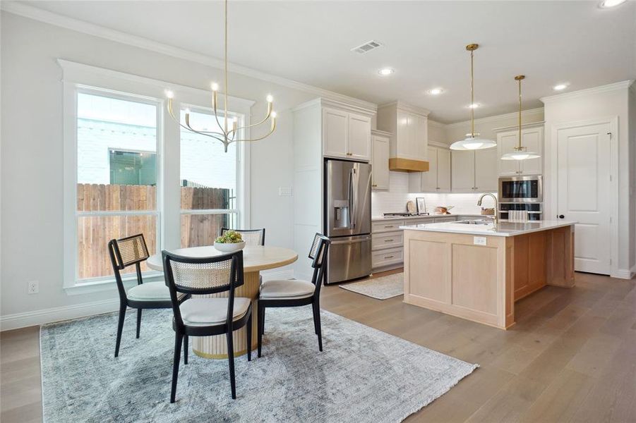Kitchen with decorative light fixtures, stainless steel appliances, a center island with sink, light hardwood / wood-style flooring, and backsplash