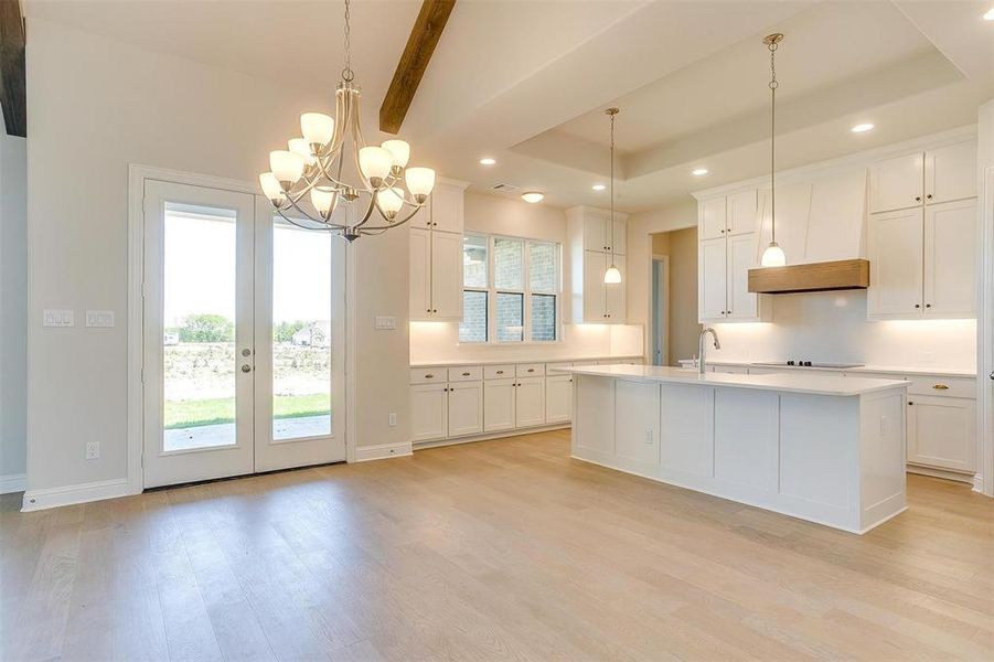 Kitchen featuring white cabinets, light hardwood / wood-style floors, a center island with sink, and a tray ceiling