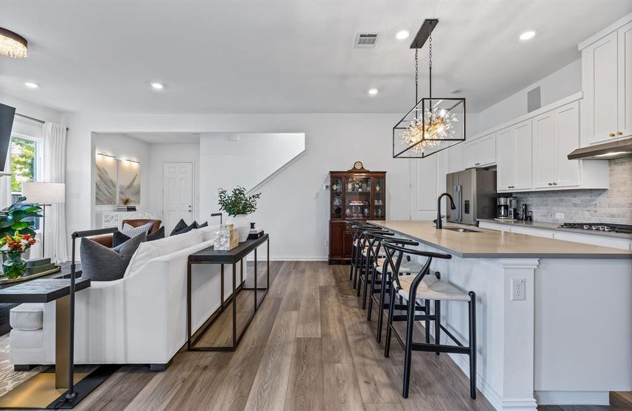 Kitchen with white cabinets, hardwood / wood-style flooring, sink, hanging light fixtures, and a center island with sink