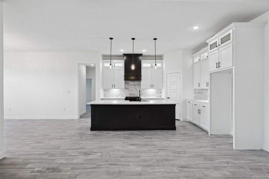 Kitchen with white cabinets, premium range hood, a center island with sink, and hanging light fixtures