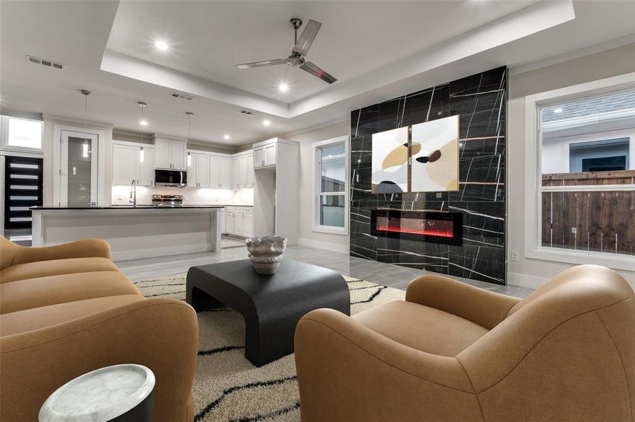 Living room featuring ceiling fan, a tile fireplace, - 24x48 fireplace porcelain tile and flooring, and a Tray ceiling