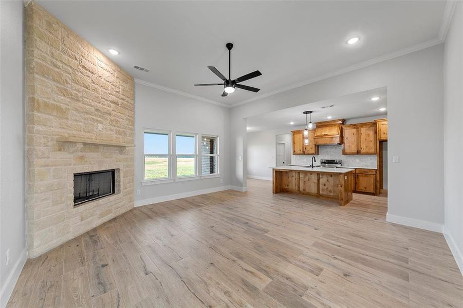 living room featuring a stone fireplace, ornamental molding, ceiling fan, and light hardwood / wood-style floors