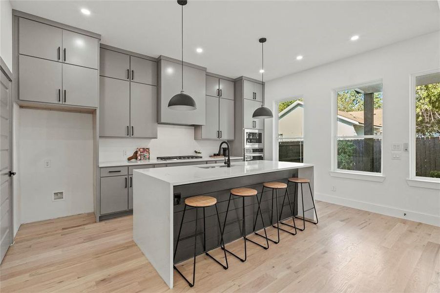 Kitchen featuring gray cabinets, a kitchen island with sink, and a breakfast bar