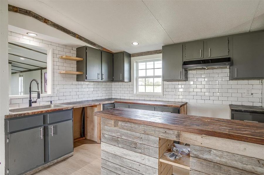 Kitchen with a textured ceiling, light hardwood / wood-style flooring, backsplash, wood counters, and sink