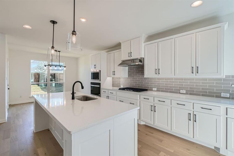 Kitchen featuring sink, light wood-type flooring, an island with sink, stainless steel oven, and white cabinetry