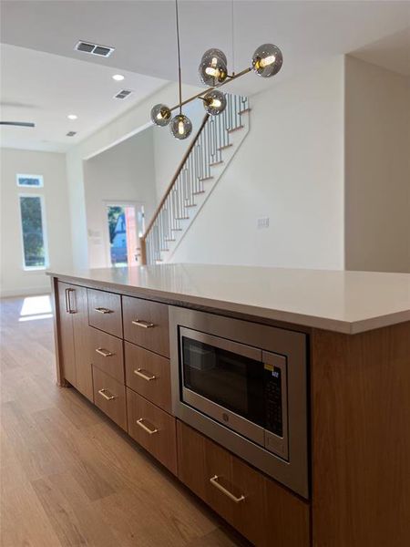 Kitchen featuring pendant lighting, stainless steel microwave, and light hardwood / wood-style floors