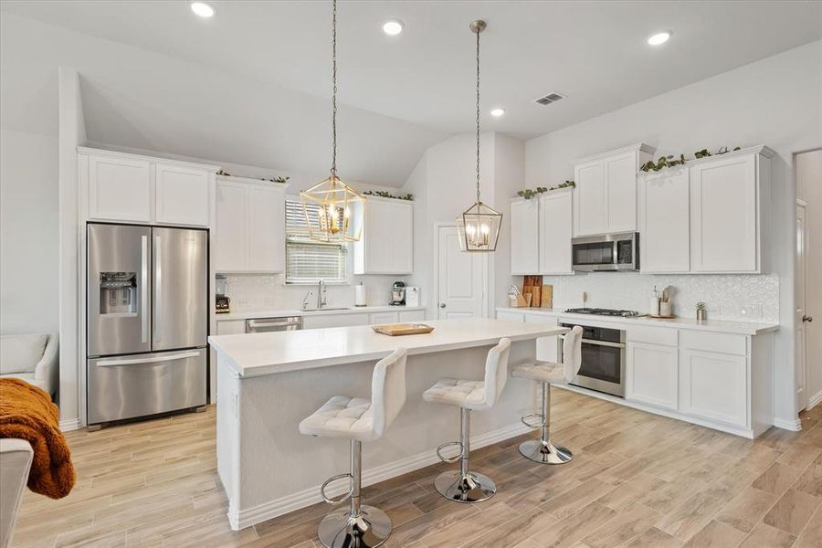 Oversized kitchen island with quartz counter tops, pendant lights, and custom white cabinets