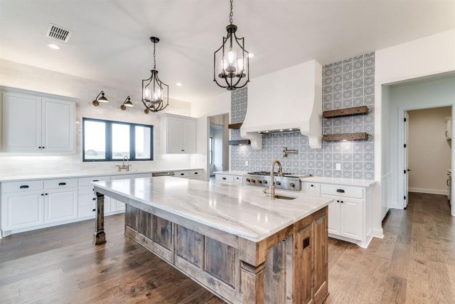 Kitchen featuring light stone countertops, a kitchen island with sink, wood-type flooring, and white cabinets