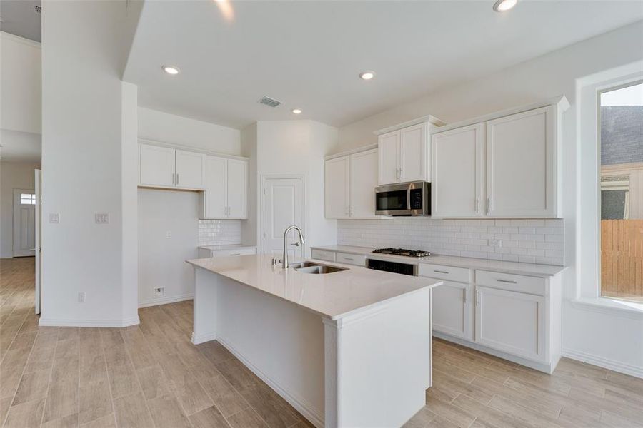 Kitchen featuring decorative backsplash, a kitchen island with sink, sink, and white cabinets