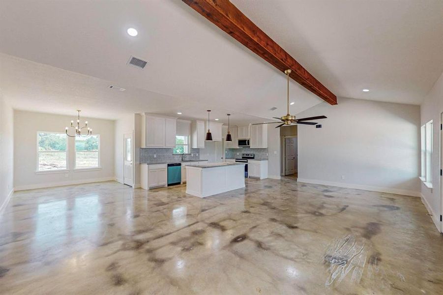 Unfurnished living room featuring ceiling fan with notable chandelier and vaulted ceiling with beams