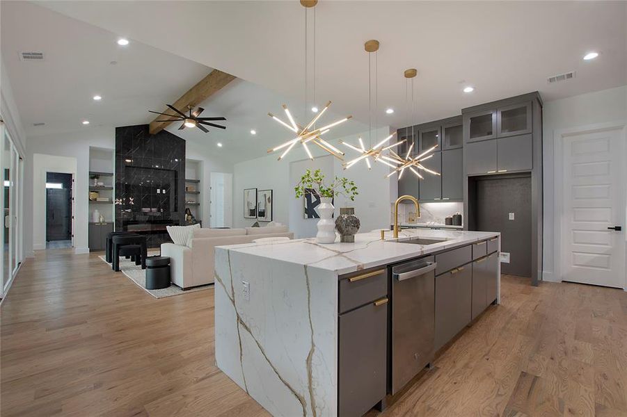 Kitchen featuring beamed ceiling, an island with sink, ceiling fan with notable chandelier, and light wood-type flooring