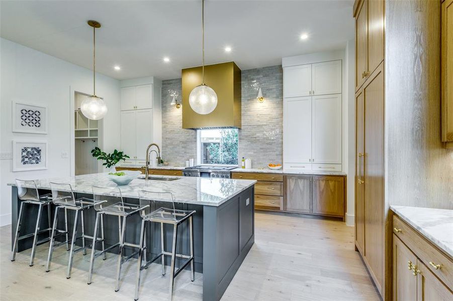 kitchen features chef appliances, designer lighting, brass wrapped vent hood, and handmade zellige tile