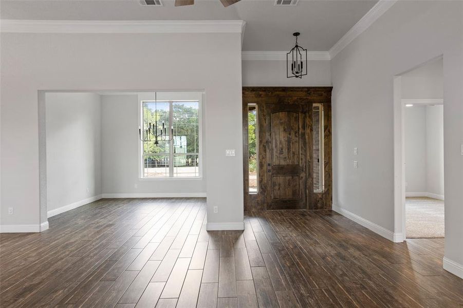 Foyer with dark hardwood / wood-style floors, crown molding, and an inviting chandelier