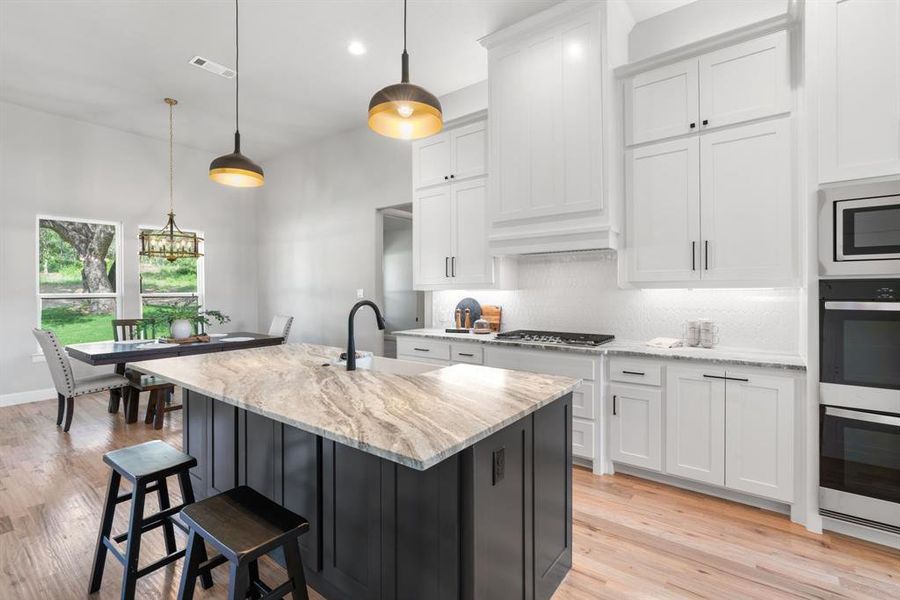 Kitchen featuring backsplash, stainless steel appliances, a center island with sink, light wood-type flooring, and pendant lighting