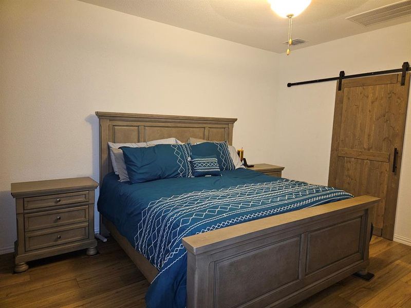 Bedroom featuring a barn door, dark hardwood / wood-style floors, and ceiling fan