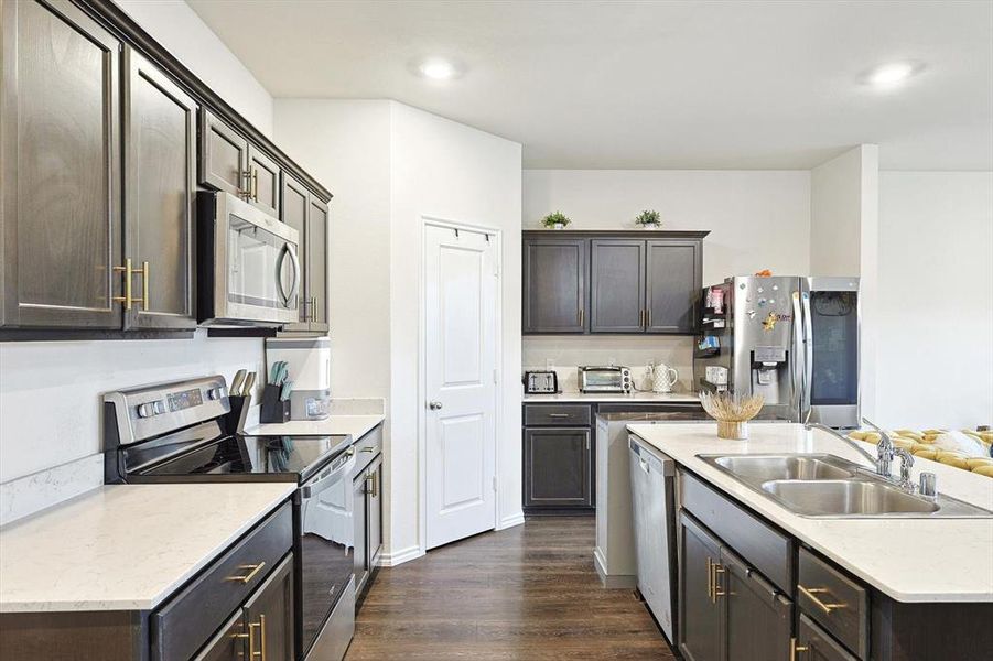 Kitchen with appliances with stainless steel finishes, sink, dark brown cabinetry, and dark hardwood / wood-style flooring