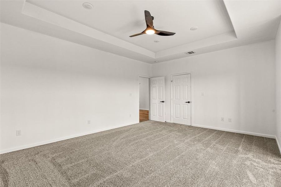 Unfurnished bedroom with carpet flooring, ceiling fan, and a tray ceiling