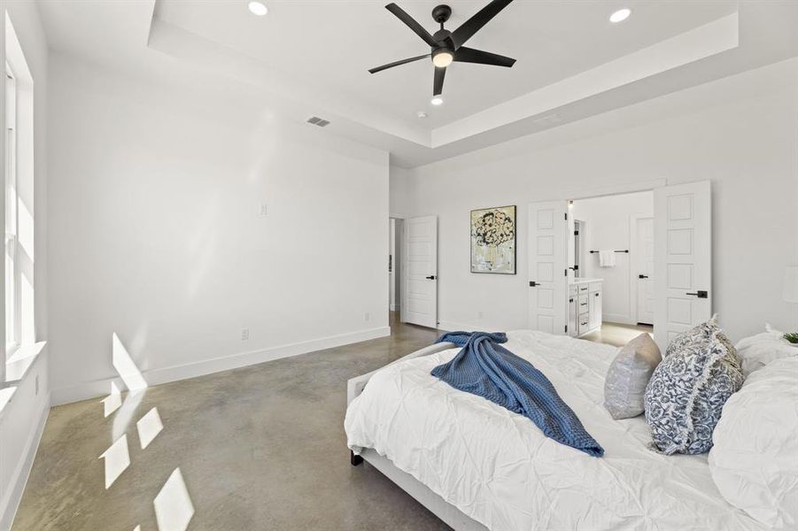 Bedroom with ceiling fan, a raised ceiling, and ensuite bath