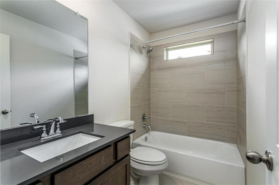 This elegant bathroom showcases a sophisticated design with its neutral tiles and sleek fixtures. The vanity provides ample storage and counter space, while the large mirror enhances the room's spacious feel. The window above the bathtub brings in natural light, adding to the bright and airy ambiance. Photos are from another Rylan floor plan.