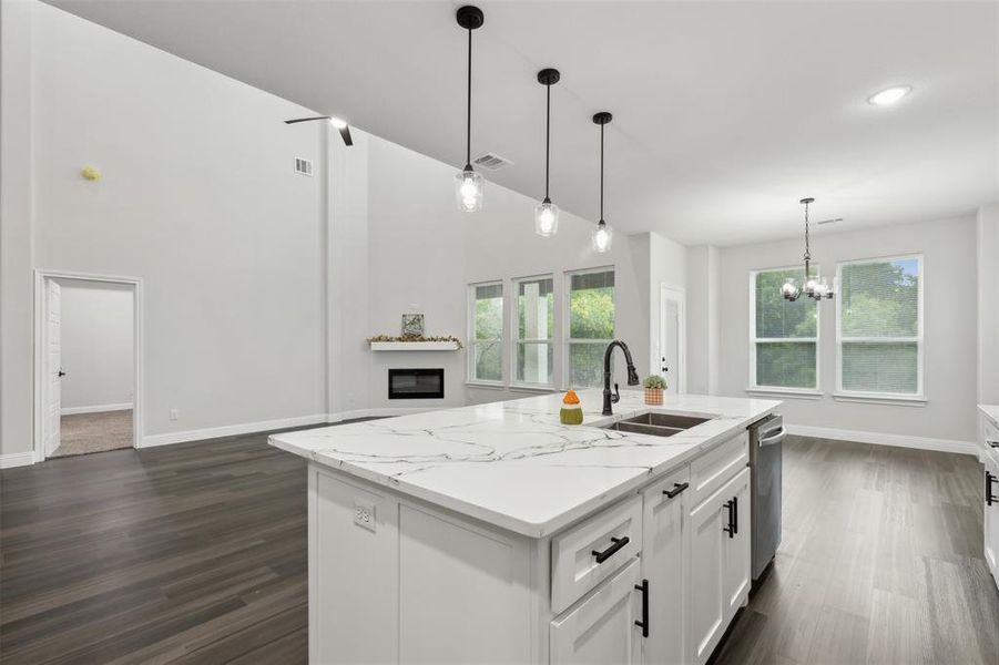 Kitchen featuring white cabinets, light stone countertops, sink, pendant lighting, and a center island with sink