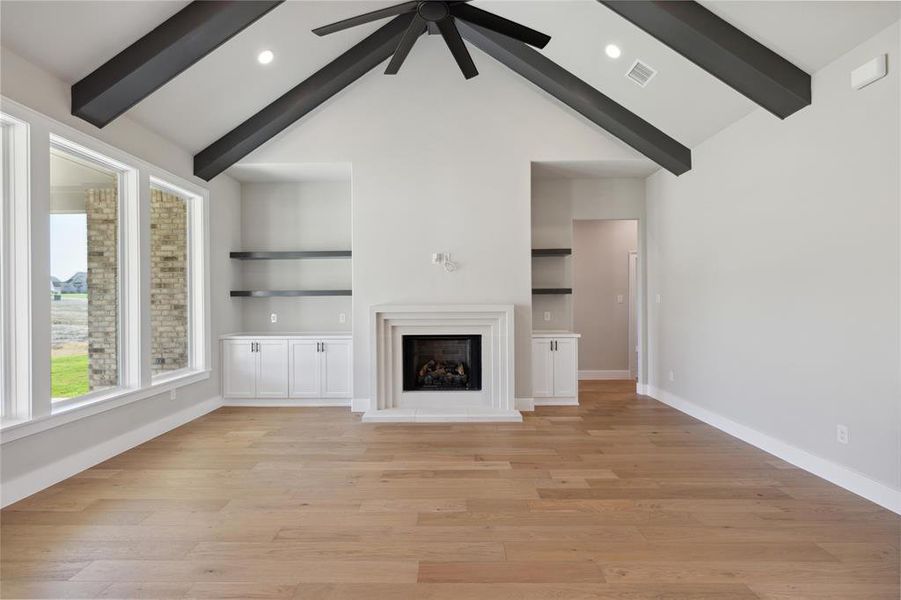 Unfurnished living room featuring light hardwood / wood-style floors, ceiling fan, and beam ceiling