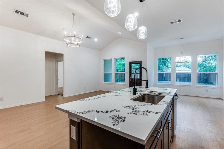 Kitchen featuring decorative light fixtures, sink, light stone countertops, a center island with sink, and light hardwood / wood-style floors