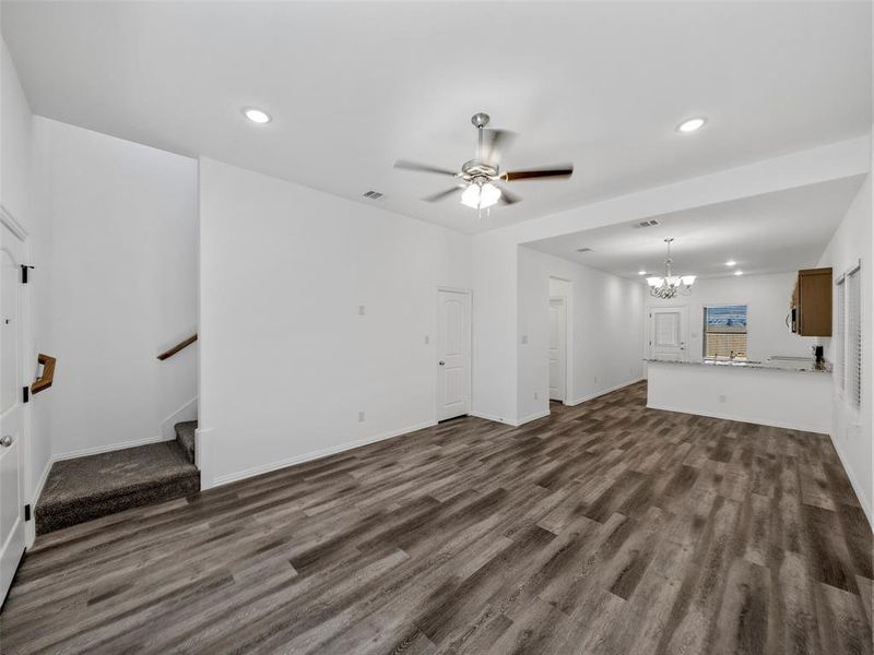 Unfurnished living room with ceiling fan with notable chandelier and dark hardwood / wood-style floors