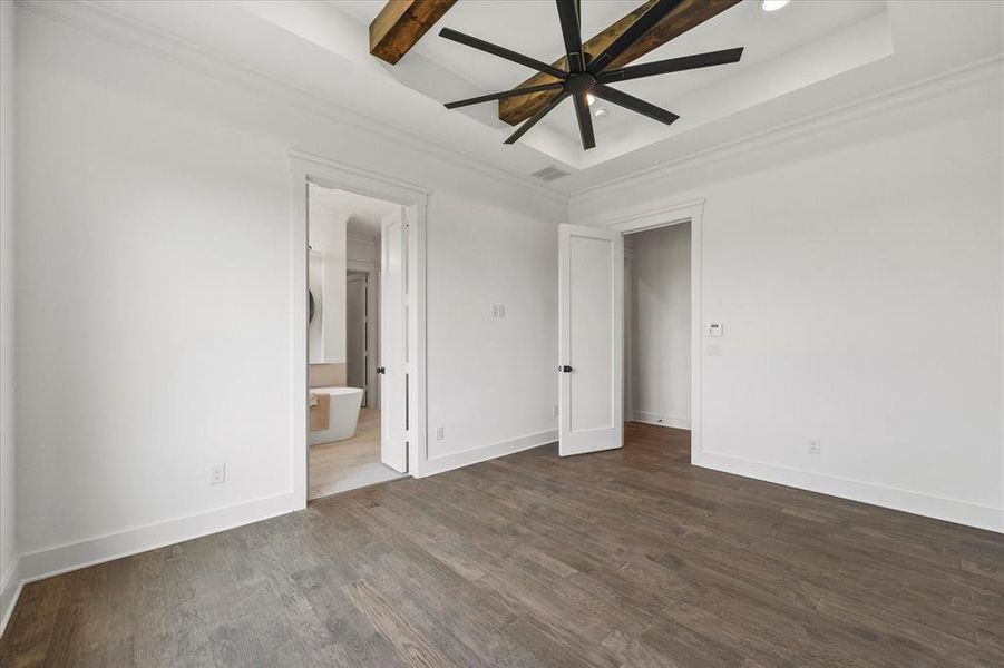 Unfurnished bedroom featuring ensuite bath, beamed ceiling, and hardwood / wood-style floors