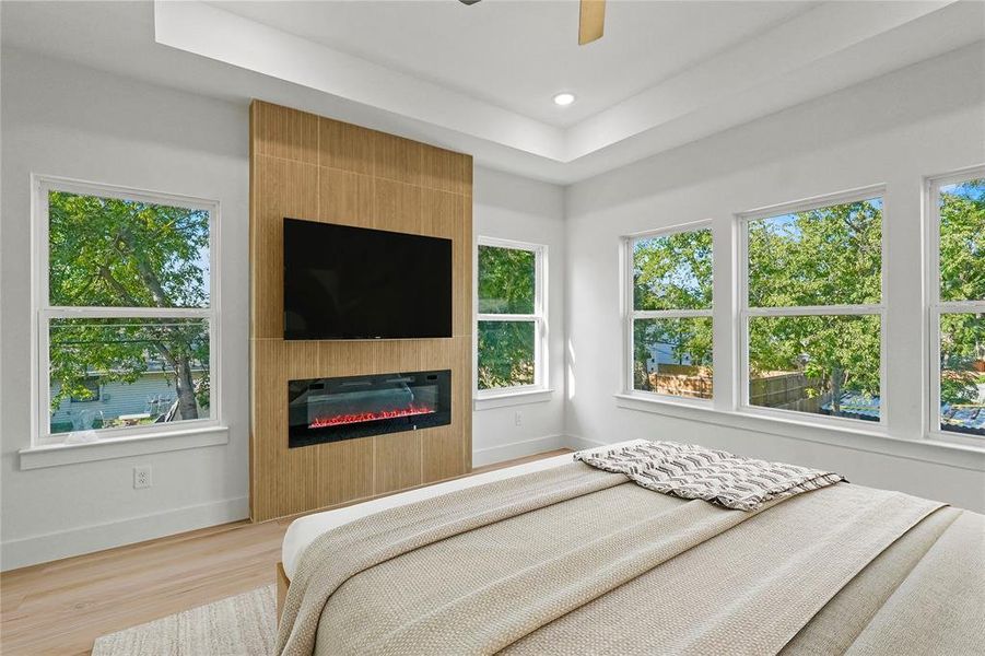 Bedroom featuring a fireplace, ceiling fan, a raised ceiling, and light hardwood / wood-style flooring